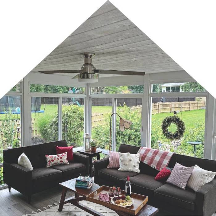 Cozy sunroom with large windows overlooking a backyard, featuring dark modern sofas, colorful throw pillows, and a wooden coffee table set for entertaining—creating a welcoming space to relax and enjoy the view year-round.