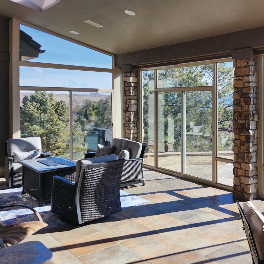 Three-season sunroom with large energy-efficient windows, stone wall accents, and wicker seating overlooking the mountains in a Denver, Colorado home.
