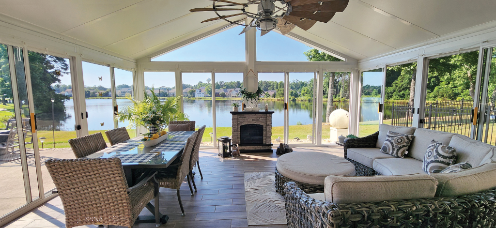 Stylish sunroom enclosure with energy-efficient windows, wicker patio furniture, ceiling fans, and a fireplace overlooking a lake in Charlotte, North Carolina